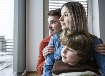 Smiling father and mother with son looking through window at home - UUF31404