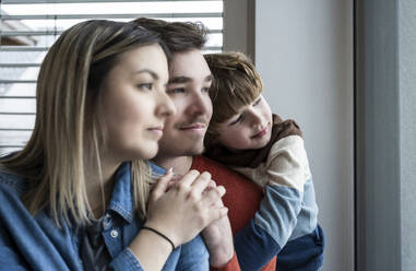 Father and mother with son looking through window at home - UUF31405