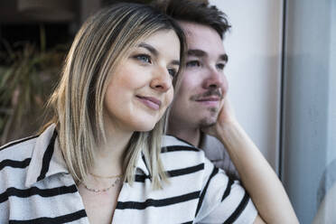 Smiling young couple looking through window at home - UUF31417