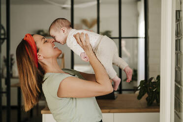 Happy mother playing with baby girl at home - EBBF08732