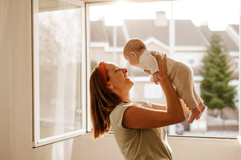 Glückliche Frau spielt mit ihrer kleinen Tochter am Fenster - EBBF08741