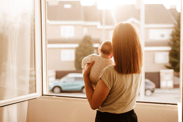 Mutter trägt ihre kleine Tochter und schaut durch das Fenster - EBBF08742