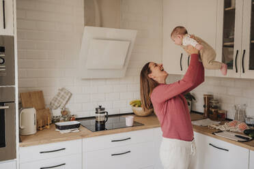 Happy woman playing with baby girl in kitchen - EBBF08748
