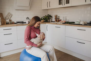 Mutter hält ihre kleine Tochter und sitzt auf einem Fitnessball - EBBF08751