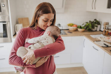 Lächelnde Frau umarmt Baby Tochter in der Küche zu Hause - EBBF08759