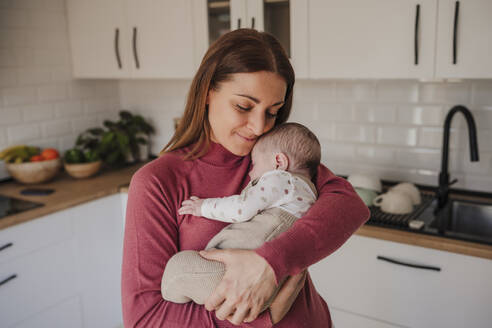 Smiling woman embracing baby daughter in kitchen - EBBF08760