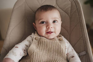 Happy cute baby girl sitting on beige bouncer chair - EBBF08783