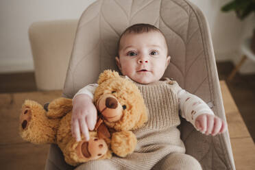 Cute baby girl sitting with stuffed toy on bouncer chair - EBBF08787