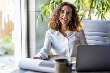 Happy businesswoman sitting at desk in office - DLTSF03758