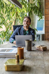 Nachdenklicher Geschäftsmann sitzt mit Laptop am Schreibtisch im Büro - DLTSF03760