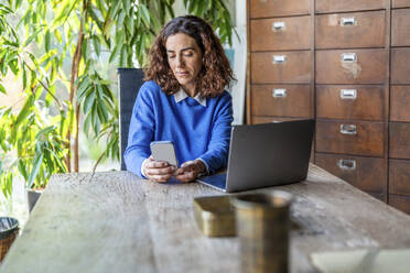 Businesswoman using smart phone near laptop in office - DLTSF03781