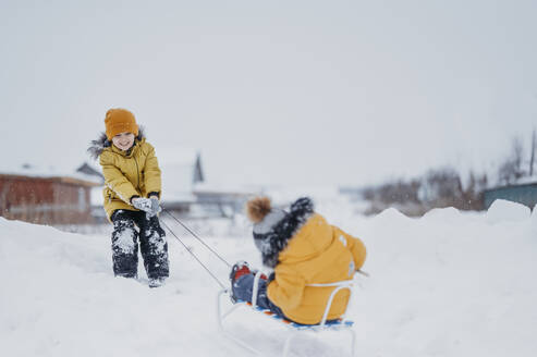 Boy pulling brother on sled in winter - ANAF02718