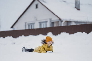 Unbekümmerter Junge im Schnee liegend im Winter - ANAF02719