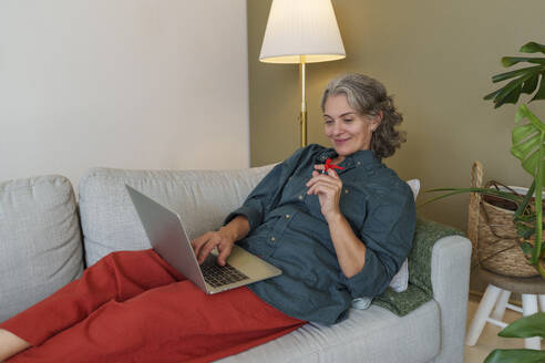 Lächelnder Freiberufler mit Erinnerungsknoten am Finger, der einen Laptop im Home Office benutzt - AAZF01529