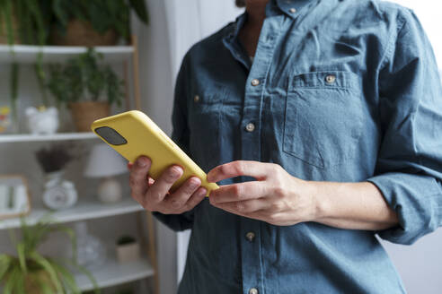 Woman wearing denim shirt and holding smart phone at home - AAZF01538