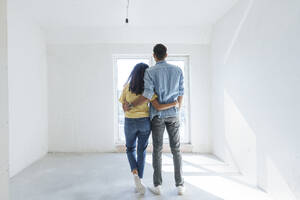 Young couple standing with arms around at new home - AAZF01543