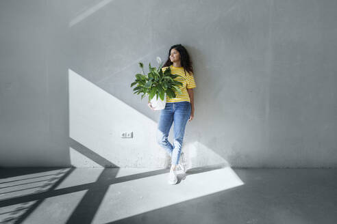 Junge Frau steht mit einer Pflanze vor der Mauer ihres neuen Hauses - AAZF01547