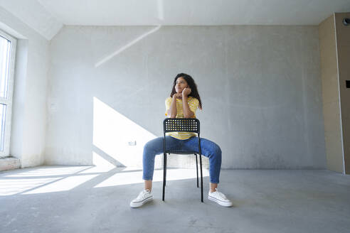 Nachdenkliche Frau sitzt auf einem Stuhl in einem renovierten Zimmer - AAZF01548