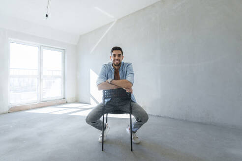 Smiling man sitting on chair in room under renovation - AAZF01549