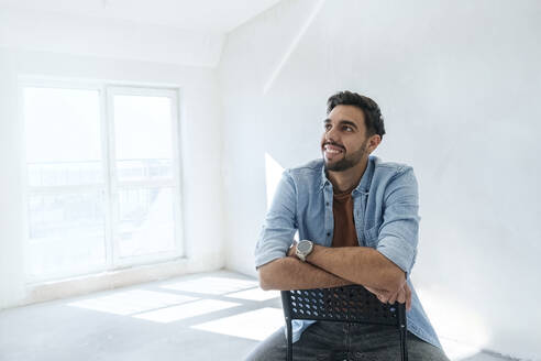 Thoughtful young man sitting on chair at new home - AAZF01550