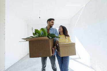 Happy young couple carrying cardboard boxes in room under renovation - AAZF01553