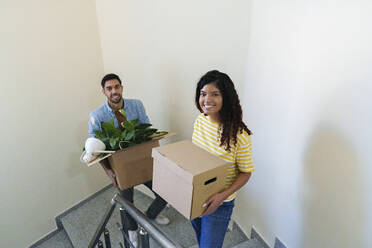 Happy couple carrying boxes on staircase at new home - AAZF01558