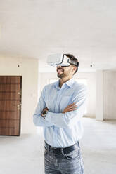Mann mit verschränkten Armen, der in einem Virtual-Reality-Simulator die Renovierungspläne für sein neues Haus analysiert - AAZF01569