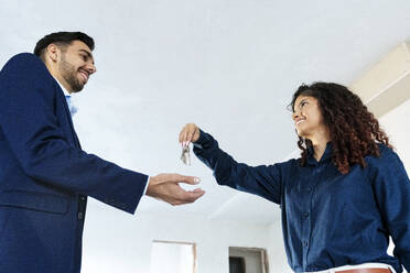 Smiling real estate agent passing keys to new owner of house - AAZF01574