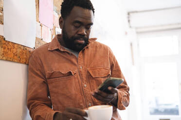 Man holding coffee cup and using smart phone at cafe - AMWF01995