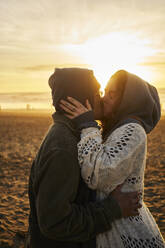 Young couple kissing on beach at sunset - ANNF00958
