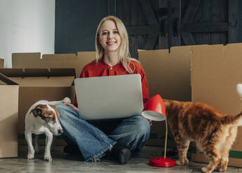 Glückliche Frau sitzt mit Haustieren und Laptop zu Hause - VSNF01673