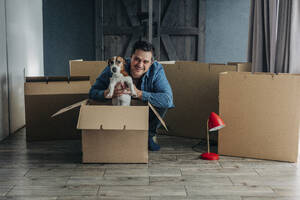 Glücklicher Mann mit Hund in der Nähe von Kartonagen zu Hause - VSNF01682