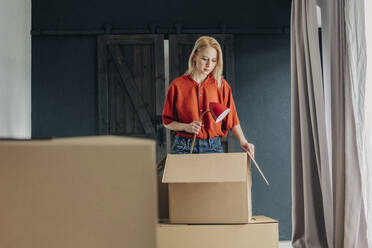 Blond woman packing lamp in box at home - VSNF01683