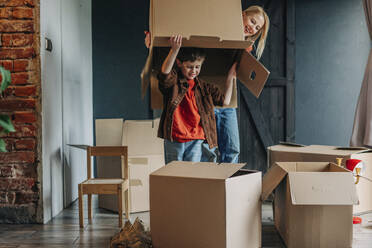 Happy woman with son holding empty cardboard box over head - VSNF01688