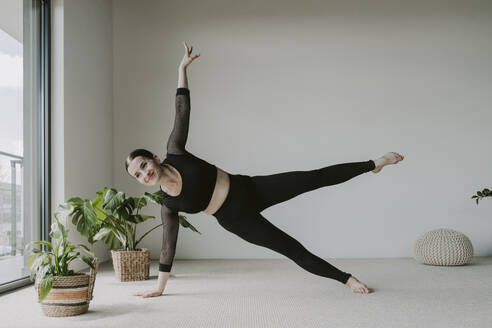 Smiling woman doing stretching exercise at home - OSF02400