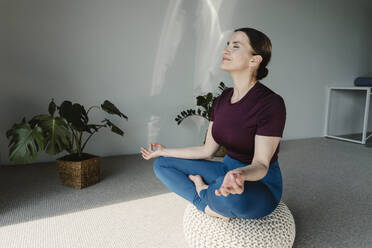 Lächelnde Frau meditiert auf einem Sitz zu Hause - OSF02415
