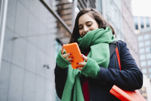 Frau mit grünem Schal und Smartphone in der Nähe eines Gebäudes - AMWF02021