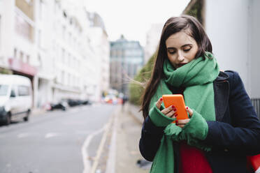 Frau trägt Schal und benutzt Smartphone auf der Straße - AMWF02022