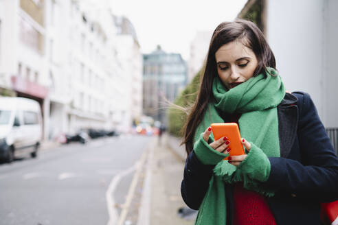 Woman wearing scarf and using smart phone on street - AMWF02022