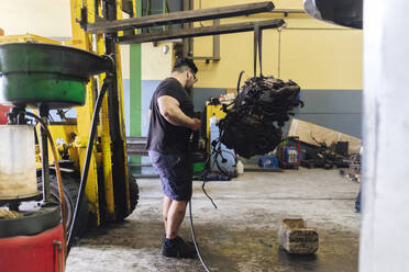 Mechaniker untersucht den Motor, der an einem Gabelstapler in der Werkstatt hängt - ASGF04895