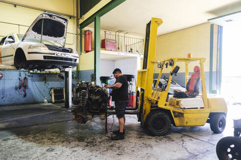 Automechaniker demontiert Motorteile in der Nähe eines Gabelstaplers in der Werkstatt - ASGF04909