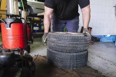 Mechanic placing vehicle tires on floor at workshop - ASGF04918
