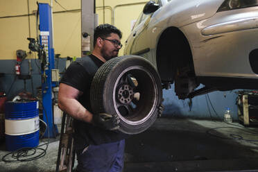 Mechanic removing tire from car at workshop - ASGF04920