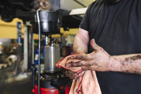 Mechaniker reinigt Hände mit Lappen in der Werkstatt - ASGF04927