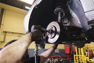 Mechanic using impact wrench to disassemble vehicle parts at workshop - ASGF04928