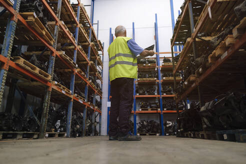 Senior auto mechanic taking standing amidst shelves at warehouse - ASGF04933
