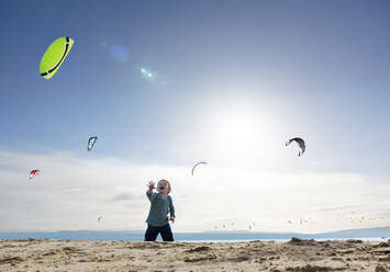Fröhlicher Junge beobachtet Kite-Surfer am Strand an einem sonnigen Tag - MBLF00268
