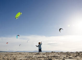 Junge spielt und beobachtet Kite-Surfer am Strand - MBLF00269