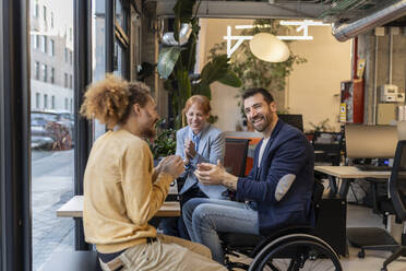 Happy manager in wheelchair applauding with colleagues at office - JCCMF11290