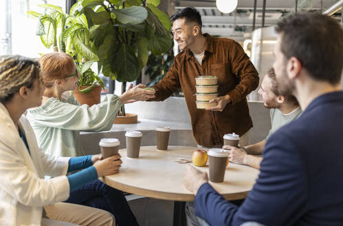 Businessman serving food to colleagues at lunch break in office - JCCMF11305